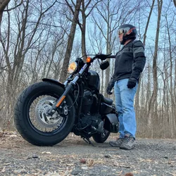 Thad in riding gear next to his motorcycle on a wooded gravel path in the evening.