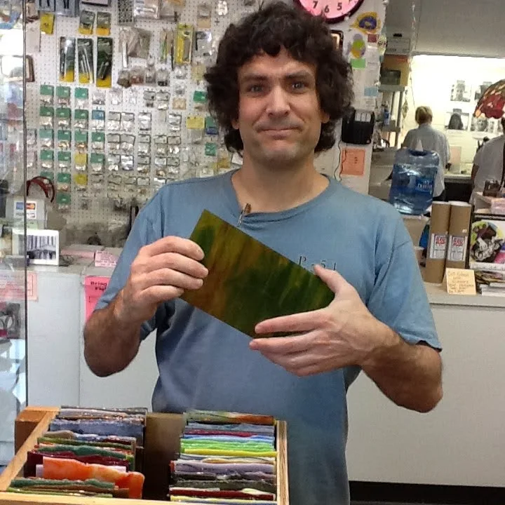 Thad holding a green stained glass sheet at a glass store