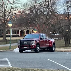 Red Ford dually pickup truck parked in a quiet lot in the early morning, with a brick building and bare trees behind it.