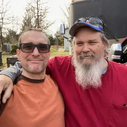 Thad with his arm around his brother Bill, both smiling outdoors.