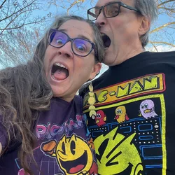 Thad and Jolynn making open-mouthed Pac-Man faces while wearing Pac-Man t-shirts outdoors.