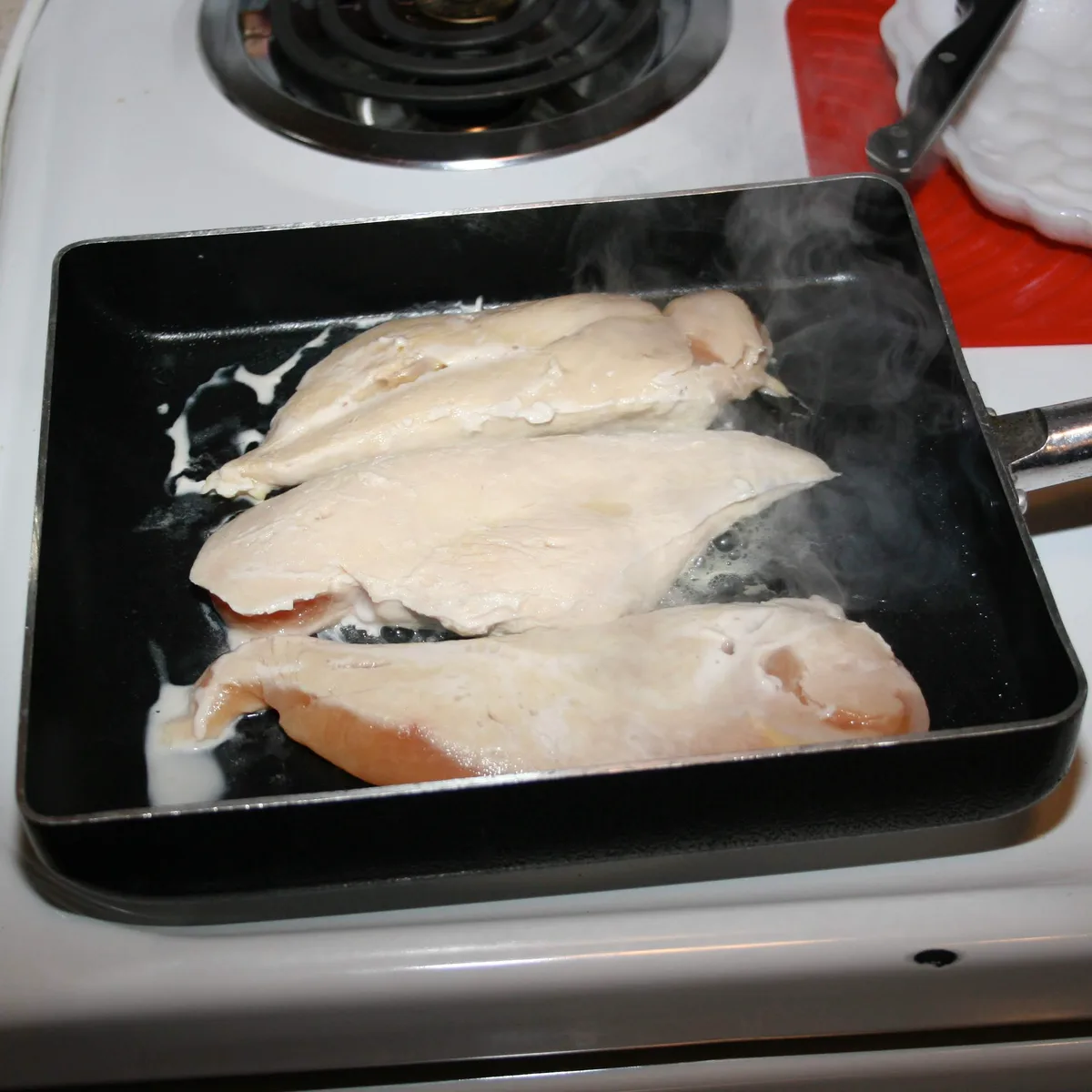 Raw chicken breasts cooking in a pan on the stove