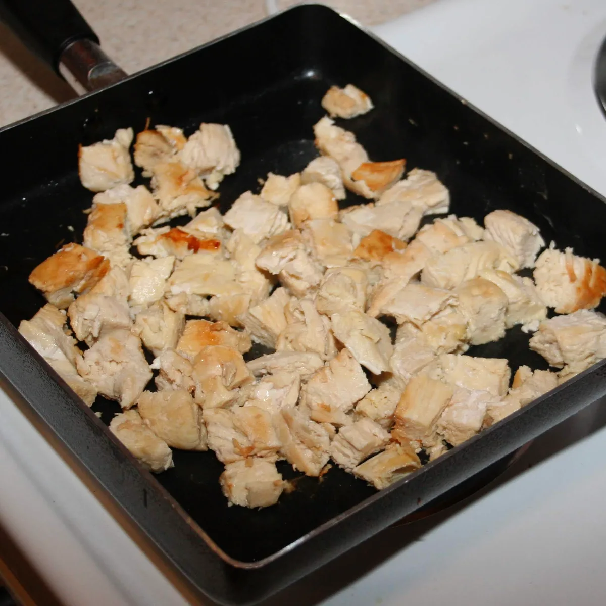 Cooked chicken cut into bite-sized pieces in a pan