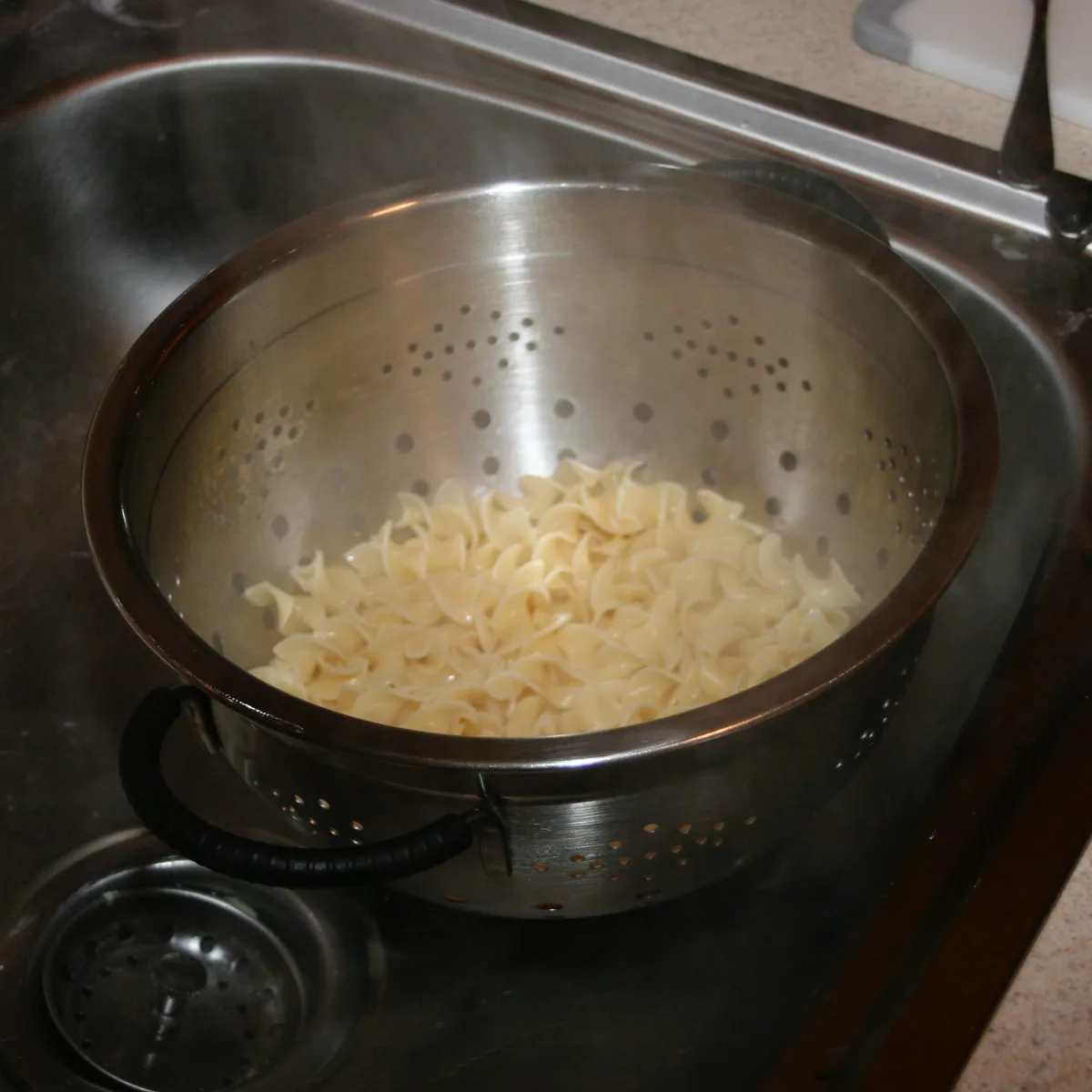 Cooked egg noodles draining in a metal colander