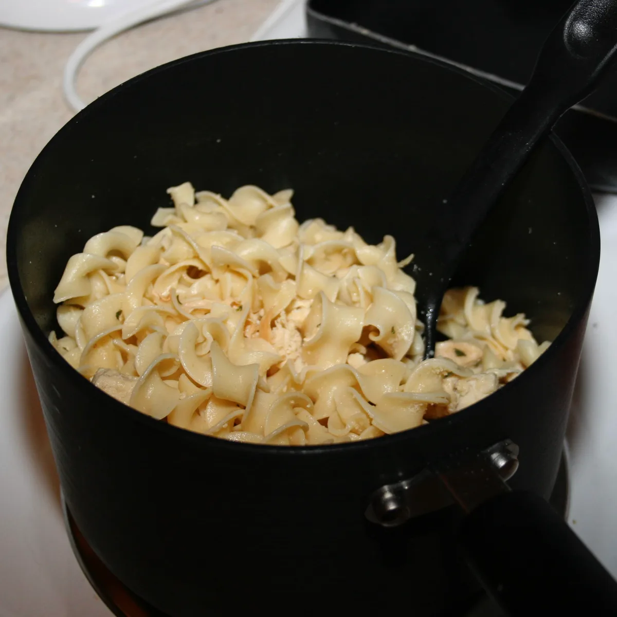 Chicken and noodles being mixed together in a pot
