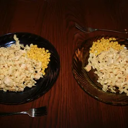 Two plates of chicken and noodles with a side of corn