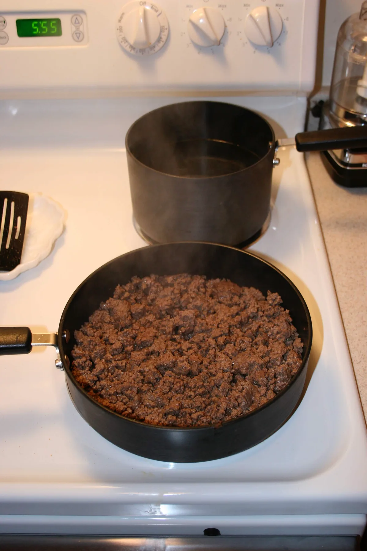 Ground beef browning in a pan next to a pot of boiling water