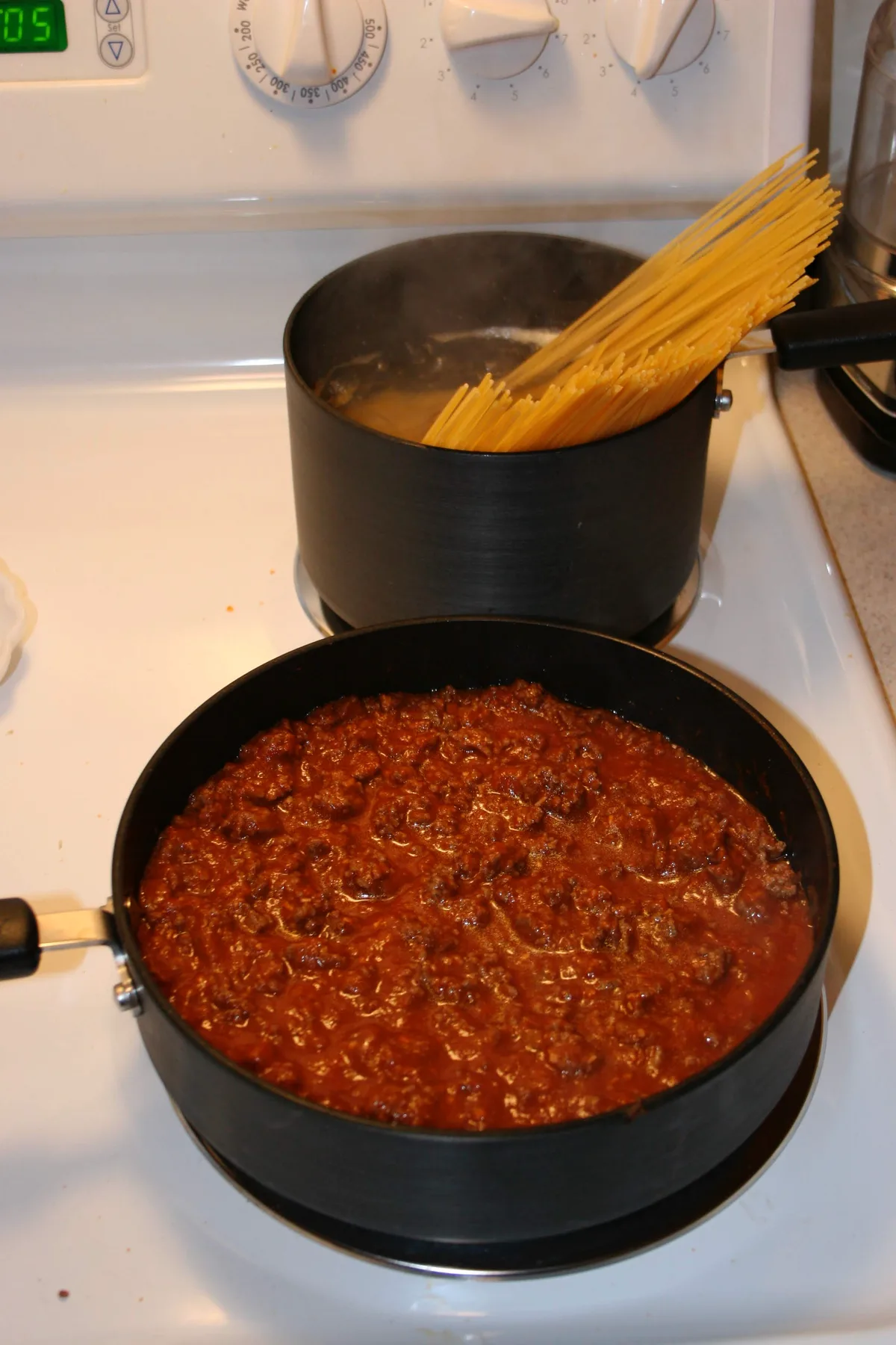 Meat sauce simmering next to spaghetti noodles being added to boiling water
