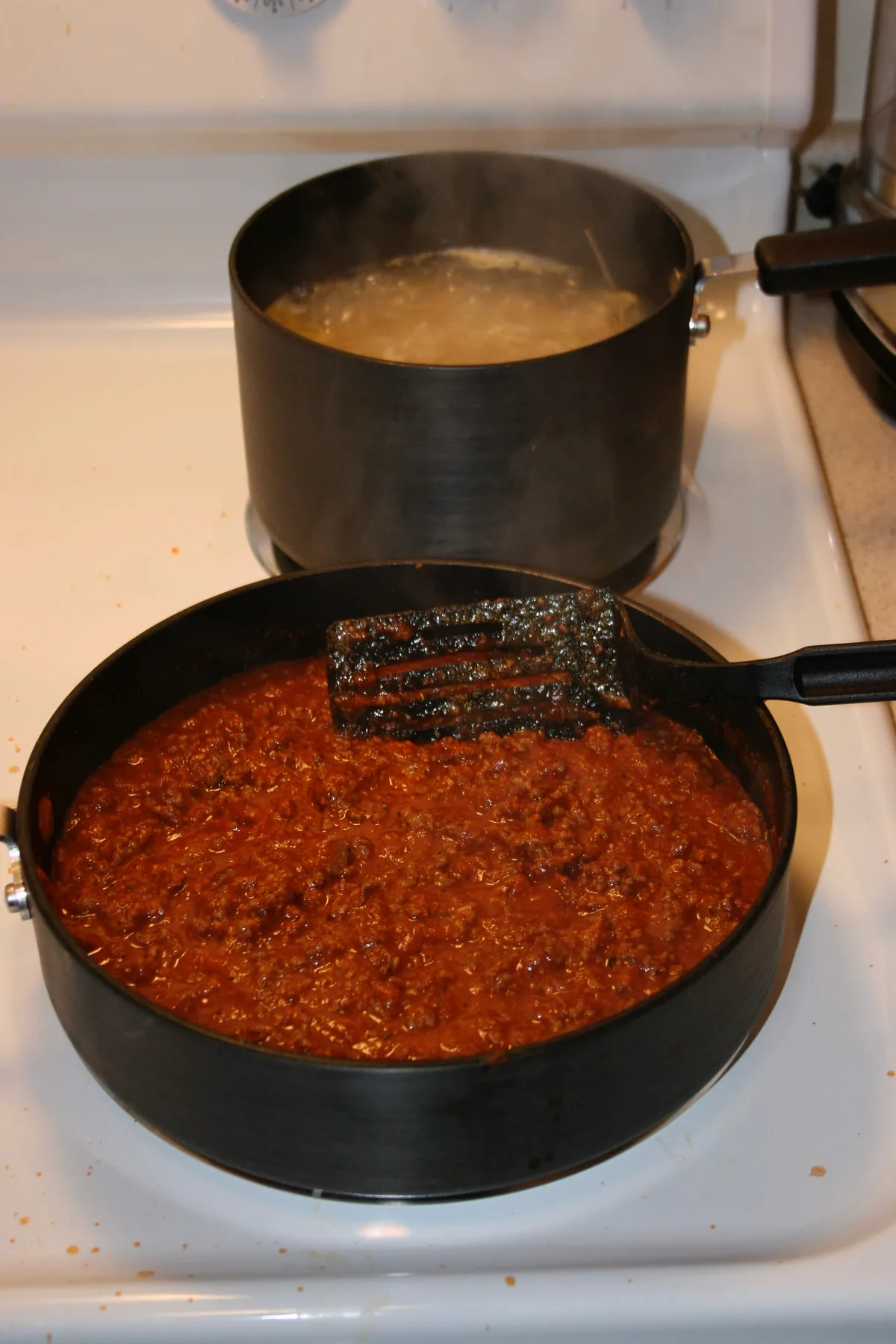 Meat sauce being stirred with a spatula next to boiling pasta