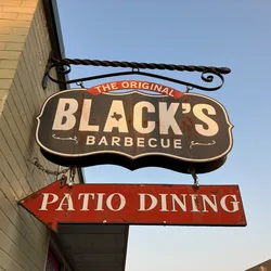 Black's Barbecue sign hanging outside the restaurant in Texas, pointing to patio dining.