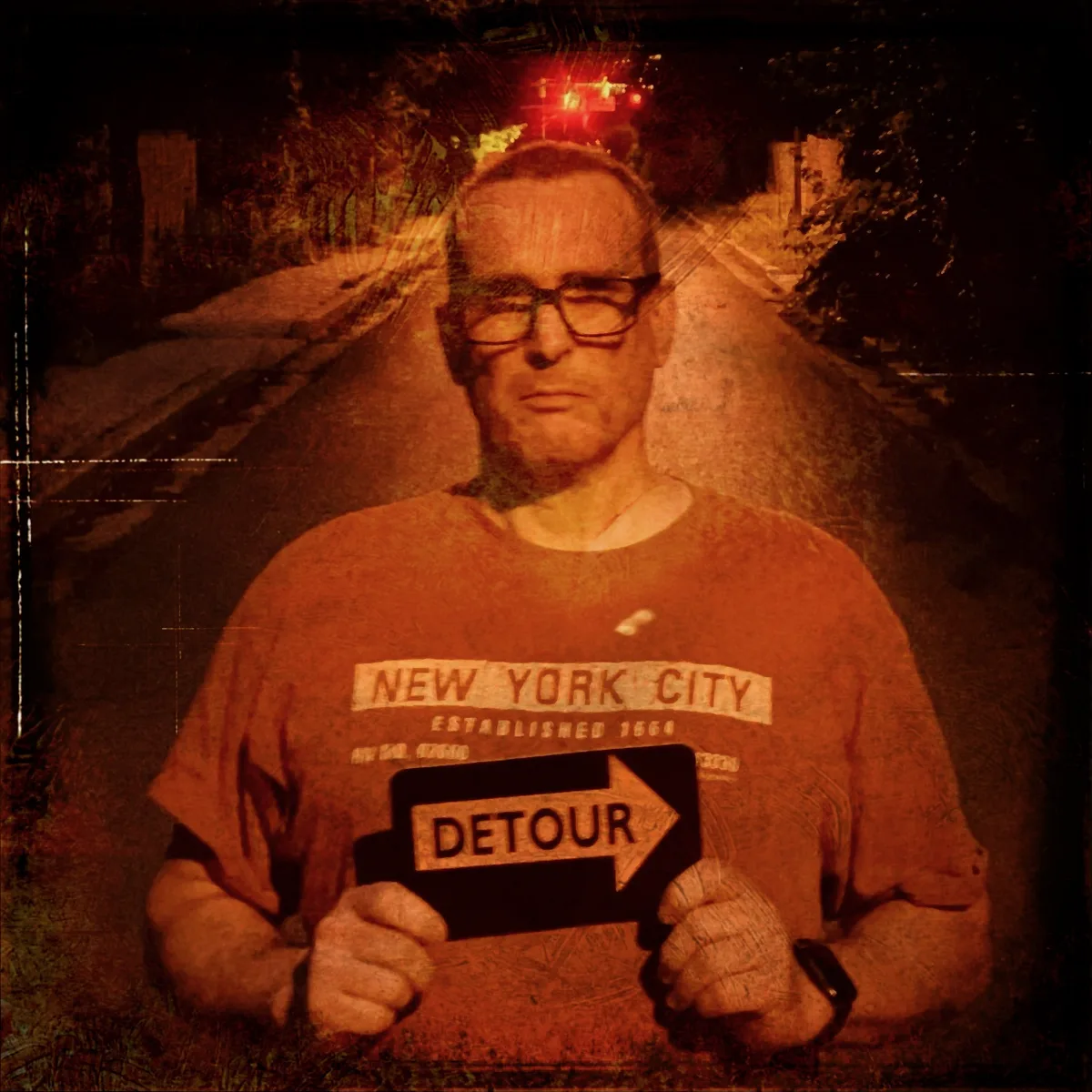 Portrait of me standing on a dimly lit road at night, holding a 'DETOUR' sign with an arrow pointing right. The image has a distressed, textured effect and red traffic lights glow in the background.