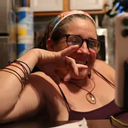 Jolynn signing "I love you" in ASL while video calling, phone propped on a stand.