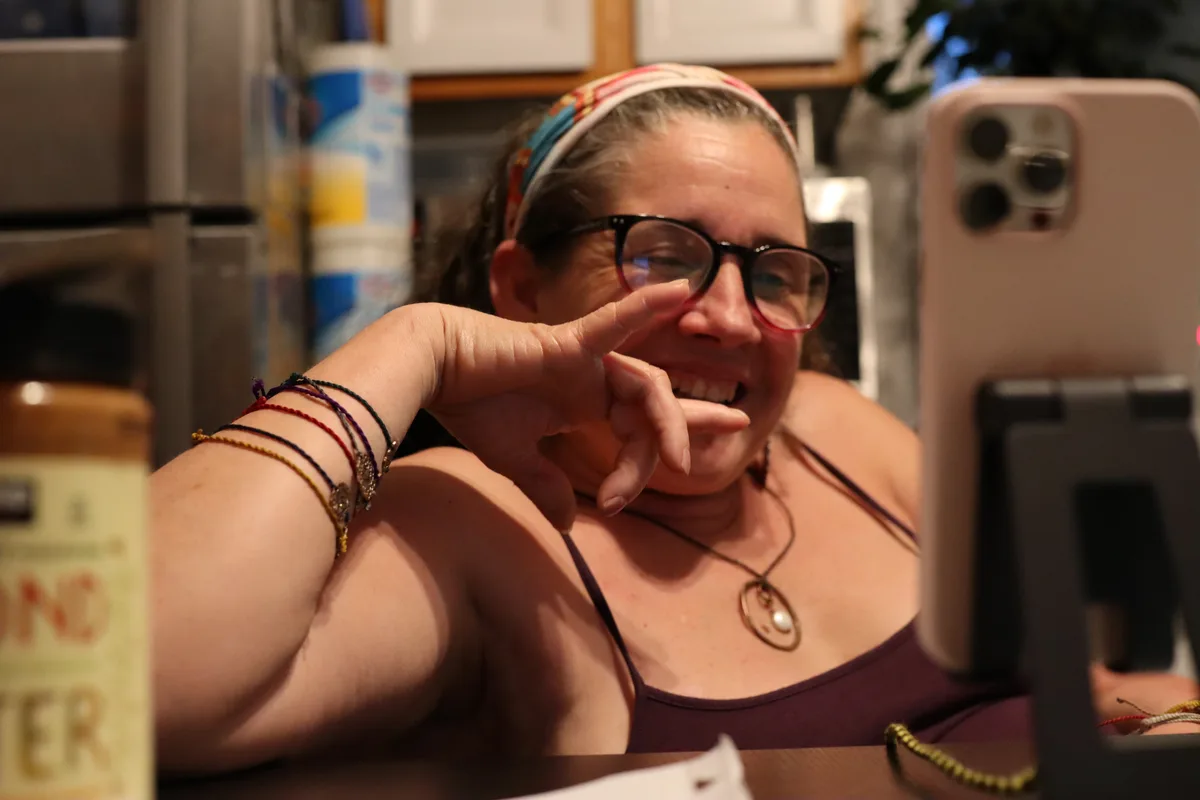 Jolynn signing "I love you" in ASL while video calling, phone propped on a stand.