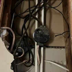 Open wall cavity showing tangled old wiring, two junction boxes, and one exposed bare wire.