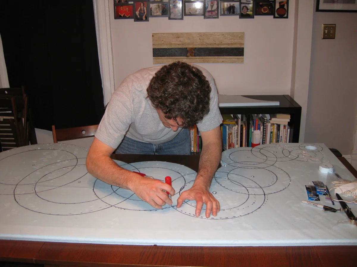 Thad leaning over a table, cutting circle shapes into foam board with an X-Acto knife.