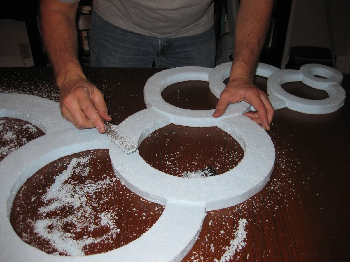 Thad rasping the edges of connected blue foam circles on a dark wood table.
