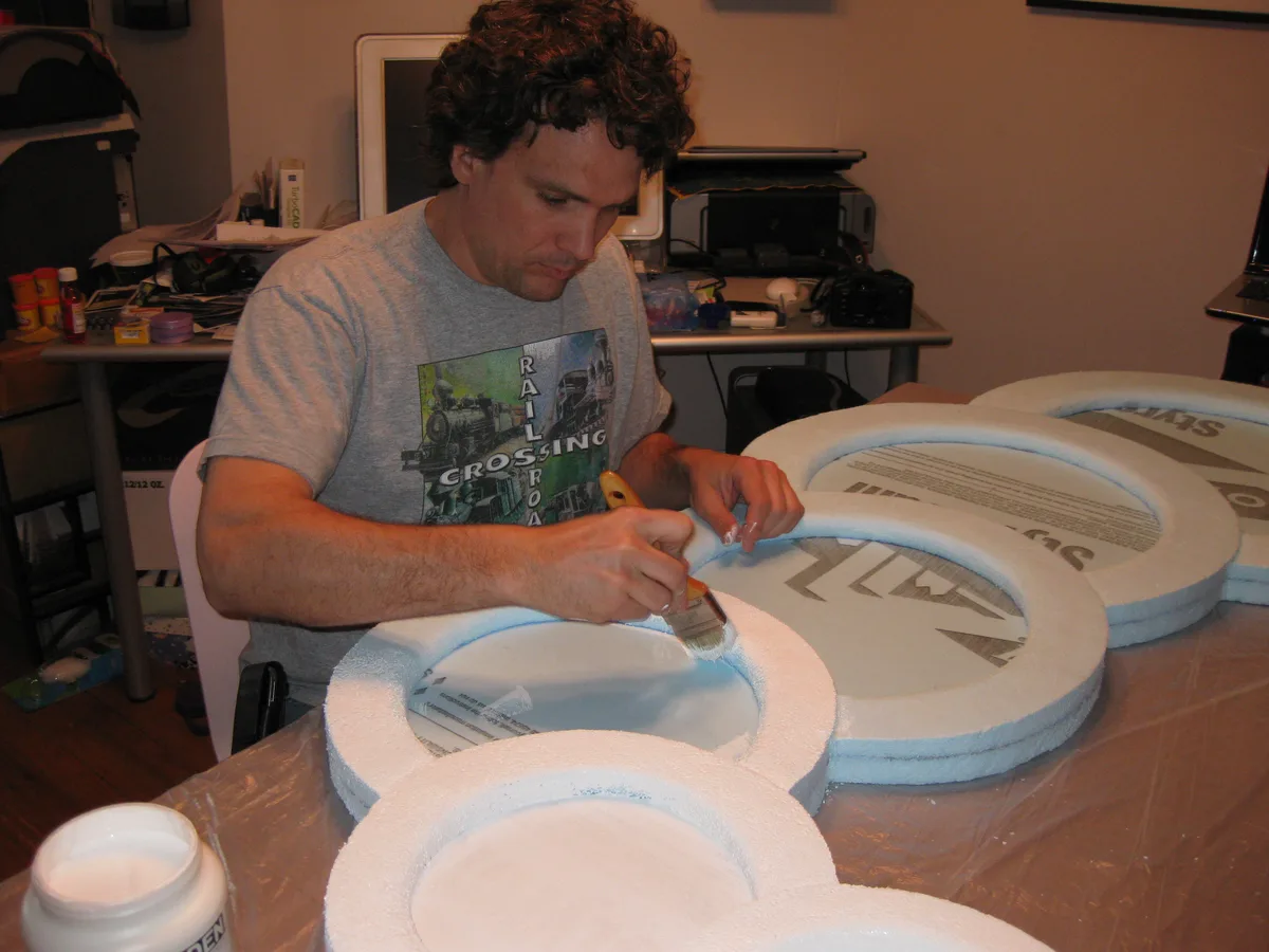 Thad brushing gesso onto a foam board at the kitchen table.