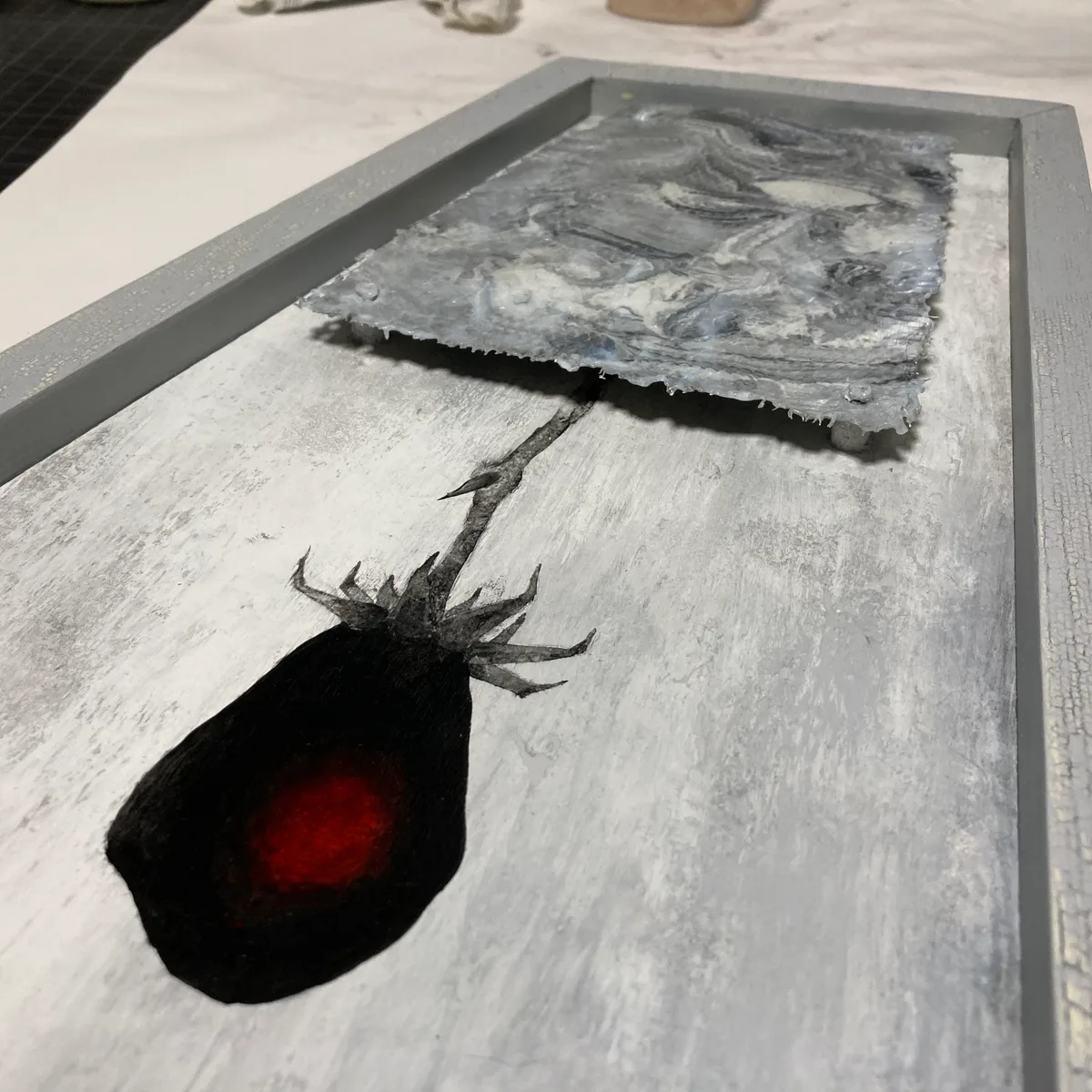 Framed panel with a dark, glowing flower form painted below, and an acrylic coated wire mesh piece mounted on standoff screws floating above it.