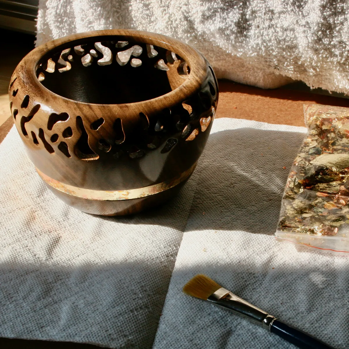 Finished walnut bowl with a bag of gold flakes and a brush nearby