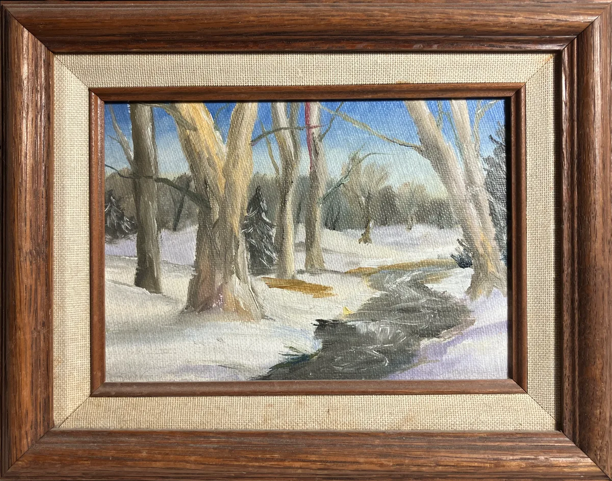Framed oil painting of a snowy forest with a stream running through it