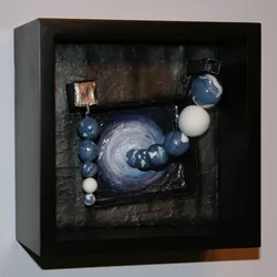 A textured mixed media artwork combining a painted spiral and layered clay beads, mounted in a black shadow box frame.