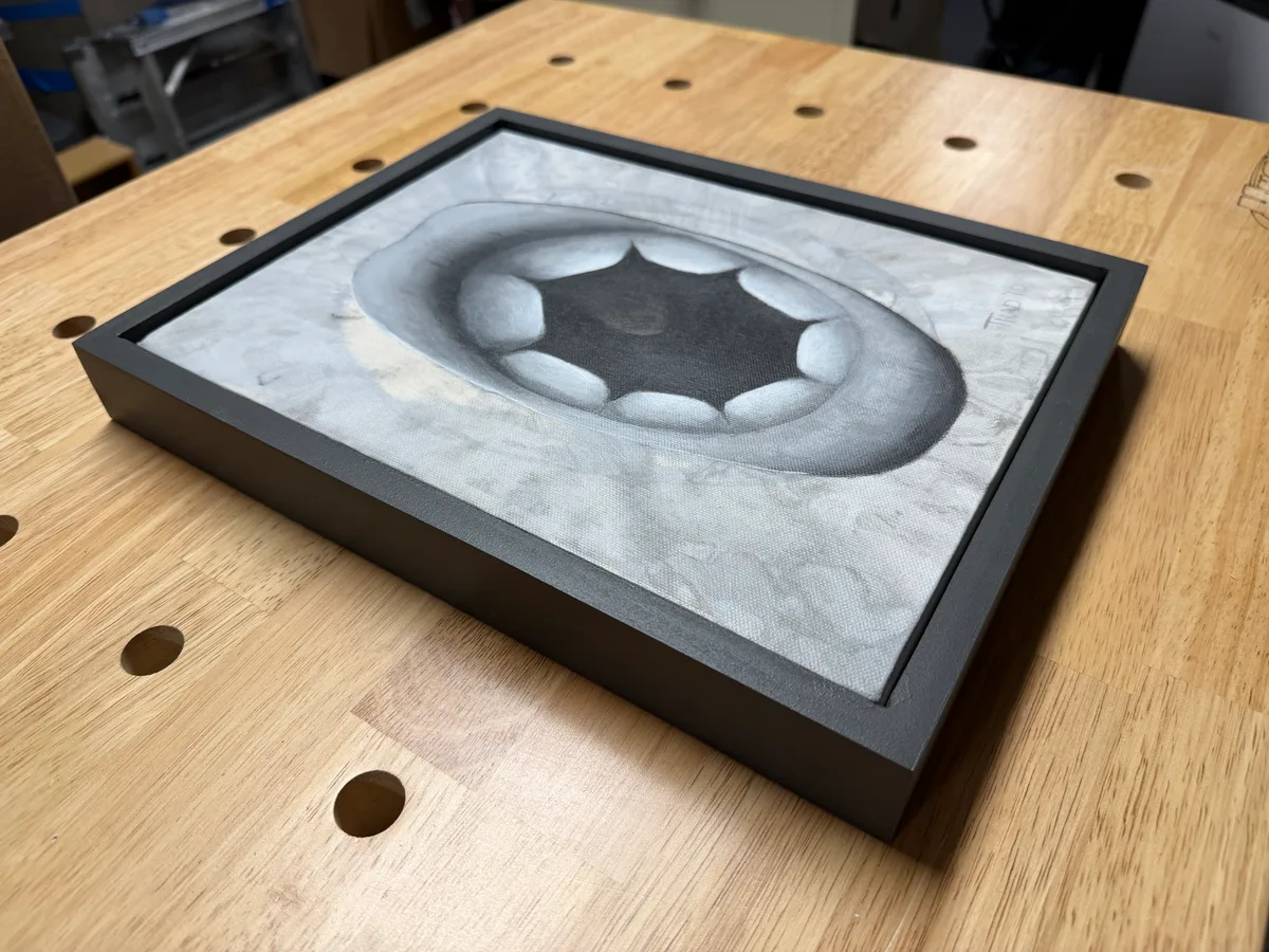 The completed painting sitting in its new black frame on a workbench.